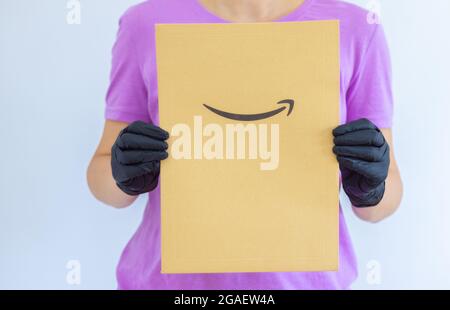 Die Hand einer Frau hält in medizinischen Handschuhen einen Papierumschlag Amazon auf weißem Hintergrund. Express-Lieferung. Der Kurier brachte das Paket Stockfoto