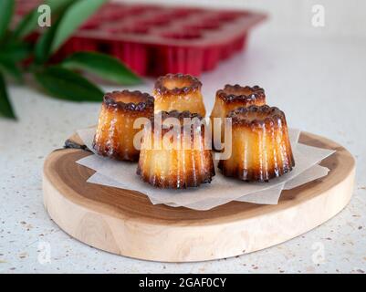 Französische Kanelen auf einem Holzbrett. Stillleben mit einem kleinen, geriffelten Gebäck mit Rum, bekannt als Canelè De Bordeaux Stockfoto