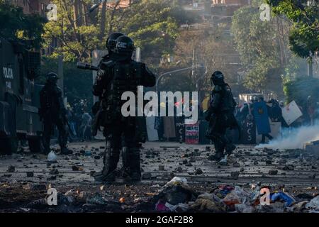 Die kolumbianischen Bereitschaftspolizisten stehen mitten in einer Straße mit Felsen und Debree, die von Demonstranten geworfen werden, als die Demonstrationen zu nächtlichen Zusammenstößen zwischen der kolumbianischen Bereitschaftspolizei (ESMAD) und Demonstranten endeten, da Kolumbien 3 Monate lang Anti-Regierungsproteste gegen die Regierung des kolumbianischen Präsidenten Ivan Duque feiert, Und eine neue Steuerreform inmitten von Unruhen und Gewalt, die seit Beginn der Proteste mindestens 83 Tote hinterlassen haben. Am 28. Juli 2021 in Medellin - Antioquia, Kolumbien. Stockfoto