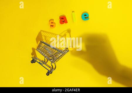 Miniatur-Einkaufswagen im Supermarkt auf gelbem Hintergrund. Die Inschrift Verkauf. Platz zum Kopieren von Text Stockfoto