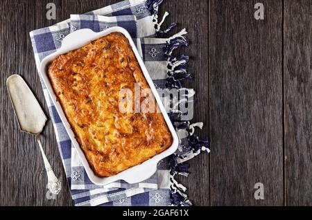 Pikante kartoffelkugel, gebackener Pudding oder Auflauf geriebener Kartoffeln in einer Auflaufform auf einem Holztisch, jüdisches Feiertagsrezept, flaches Lay, Freiraum Stockfoto