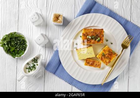 kartoffelkugel, gebackener Pudding oder Auflauf geriebener Kartoffeln auf einem weißen Teller auf einem weißen Holztisch, jüdisches Feiertagsrezept, flaches Lay Stockfoto