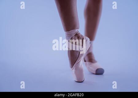 Die Füße der Balletttänzerin in spitzenschuhen aus der Nähe, sie posiert auf Zehenspitzen isoliert auf blauem Studiohintergrund. Die Beine einer schönen Frau. Nicht Erkennbar Stockfoto