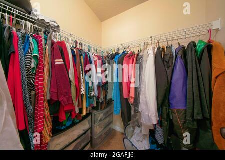 Kleiner begehbarer Kleiderschrank mit bunten Kleidern an Metallstangen Stockfoto