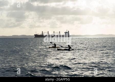 Salvador, Bahia, Brasilien - 21. März 2021: Menschen in zwei Kajaks segeln in der Bucht aller Heiligen neben einem großen Schiff. Stockfoto