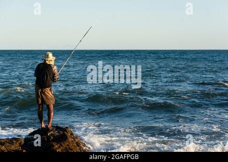 Salvador, Bahia, Brasilien - 25. April 2021: Fischer auf den Felsen, der mit seinem Angelstock fischt. Red River Beach. Stockfoto