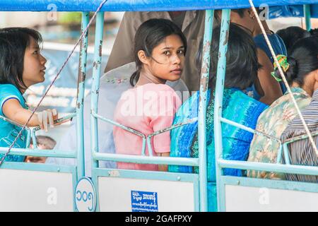 Sehr hübsches, junges burmisches Mädchen, das in einem lokalen Bus unterwegs ist, blickt über ihre Schulter auf die Kamera Yangon, Myanmar Stockfoto