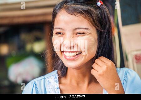 Sehr hübsches burmesisches Mädchen mit Thanaka-Gesichtspuder auf Wangen mit perelförmigen weißen Zähnen lachend, Yangon, Myanmar Stockfoto