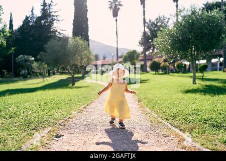 Das kleine Mädchen läuft auf einem Schotterweg in einem grünen Park Stockfoto