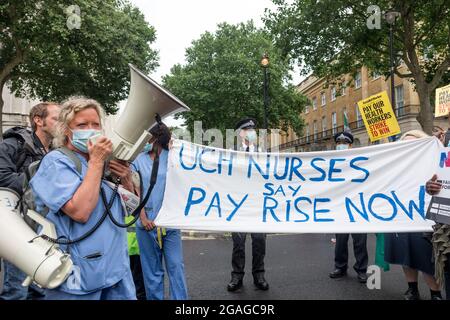 Janet Maiden (L), Krankenschwester spricht mit einem Megaphon vor einem Transparent mit der Aufschrift "UCH Nurses Say Pay Rise Now" während einer Demonstration vor der Downing Street.Mitglieder des National Health Service (NHS) versammelten sich vor dem St. Thomas' Hospital, bevor sie in einer Demonstration in Richtung Downing Street marschierten und faire Bezahlung forderten NHS-Arbeitnehmer, da die revidierte Gehaltserhöhung um 3 % der Regierung als kaum zufriedenstellend angesehen wurde. Zu den angesprochenen Themen gehörten lange Arbeitszeiten, Unterpersonal und der Mangel an geeigneten Schutzmaterialien für die Beschäftigten im Gesundheitswesen. Die Demonstration wurde von NHS-Arbeitern geführt, sagen sie Stockfoto