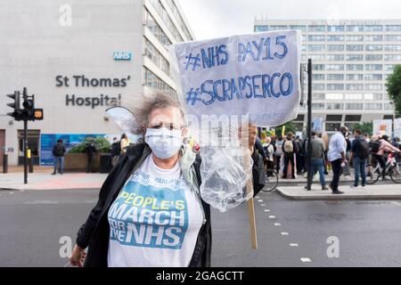 Eine Krankenschwester im Ruhestand, die ein Hemd trägt, in dem steht, dass „der marsch der Menschen für den NHS“ steht, trägt ein Schild mit der Aufschrift „NHS Pay15, Während der Demonstration vor dem St. Thomas' Hospital kratzen Sie serco'.Mitglieder des National Health Service (NHS) versammelten sich vor dem St. Thomas' Hospital, bevor sie in einer Demonstration in Richtung Downing Street marschierten, um eine faire Bezahlung für die Beschäftigten des NHS zu fordern, da die revidierte Gehaltserhöhung von 3 % der Regierung kaum als zufriedenstellend angesehen wurde. Zu den angesprochenen Themen gehörten lange Arbeitszeiten, Unterpersonal und der Mangel an geeigneten Schutzmaterialien für die Beschäftigten im Gesundheitswesen. Die Demonstration wurde von NHS-Mitarbeitern geführt, die Nein sagen, Stockfoto