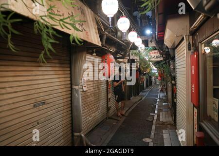 Tokio, Japan. Juli 2021. Ein Mann mit Gesichtsmaske überprüft sein Mobiltelefon in einer Gasse mit geschlossenen Geschäften gemäß den Bestimmungen des US-Bundesstaates Emergency. Die Geschäfte werden gebeten, um 8 Uhr ihre Türen zu schließen und keinen Alkohol zu servieren. 3300 Menschen haben während des Ausnahmezustands in Tokio am achten Tag der Olympischen Spiele 2020 in Tokio positiv auf das neuartige Coronavirus (Covid-19) getestet. (Foto: Stanislav Kogiku/SOPA Images/Sipa USA) Quelle: SIPA USA/Alamy Live News Stockfoto