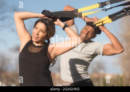 Sportliche Partner trainieren Bizeps und Arme mit trx-Fitnessbändern im Park Stockfoto