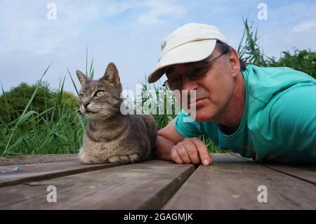 Ein Mann mit einer entzückenden Tabby-Katze auf einer Holzterrasse im Garten Stockfoto