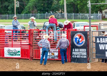 Cowboys unterstützen einen Bullenfahrer, während er sich auf ein Bullenreiten-Event auf dem Noble County Fairgrounds in Kendallville, Indiana, USA, vorbereitet. Stockfoto