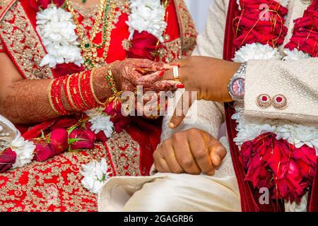 Die Braut mit Brautschmuck und Henna-Dekoration auf der Hand befestigt den Ring am Finger des Bräutigams bei der traditionellen religiösen Zeremonie bei einer hinduistischen Hochzeit Stockfoto