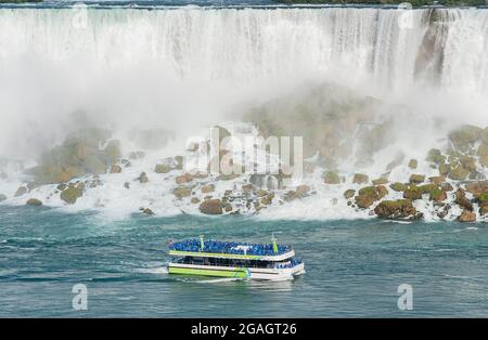 Das Boot der Maid of the Mist Tour wird neben den American Falls gezeigt, wie es von den Niagara Falls, Ontario, Kanada, aus gesehen wird. Stockfoto