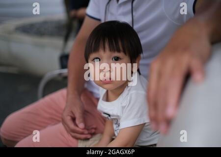 Ein junger thailändischer Junge schaut zur Kamera, während er vom Vater umarmt wurde Stockfoto