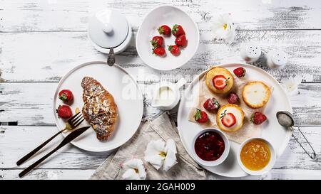 Lebensmittelbanner. Appetitliche knusprige Croissants und Pfannkuchen mit Hüttenkäse, frischen Erdbeeren und süßer Beerenmarmelade. Leckeres und gesundes Frühstück. Sw Stockfoto