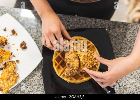 Draufsicht auf die Hände einer Frau, die gebratenes Huhn auf Waffeln und Sirup übertünchen Stockfoto