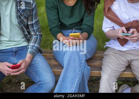 Gruppe junger Menschen, die auf dem Behcn sitzen und Smartphones in den Händen halten Stockfoto