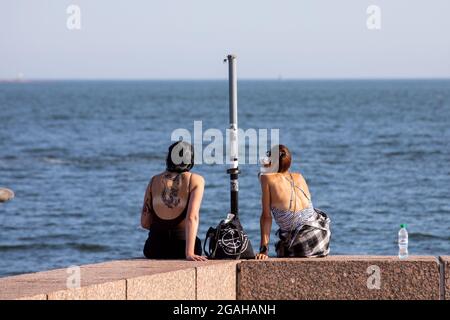 Zwei Frauen sitzen an einem warmen Sommerabend auf dem Dock im finnischen Eira-Viertel Stockfoto