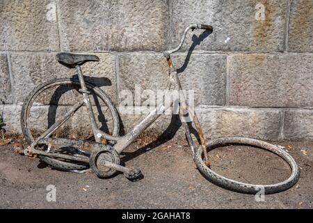 Fahrradwrack, das aus dem Fluss gerettet wurde und sich an einer Steinmauer stützte Stockfoto