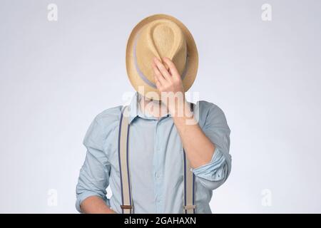 Ein junger Mann in blauem Hemd bedeckte seine Augen mit einem Sommerhut Stockfoto
