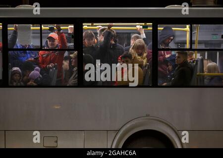 Tula, Russland - 9. Mai 2021: Menschenmenge in weißem öffentlichen Bus in Frühlingsnacht, Seitenansicht von außen. Stockfoto