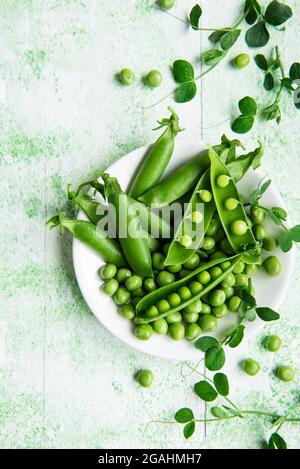 Frische grüne Erbsen-Schoten und grüne Erbsen mit Sprossen auf grünem Holzhintergrund. Konzept der gesunden Ernährung, frisches Gemüse. Stockfoto