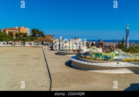 Barcelona, Spanien - 12. April 2021 - ein Blick auf die Menschen auf dekorierten Gaudi-Bänken im Parque Güell mit dem Stadtbild von Barcelona im Hintergrund Stockfoto