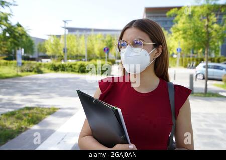 Schöne Student Mädchen trägt FFP2 Schutzmaske zu Fuß in der modernen Straße Stockfoto