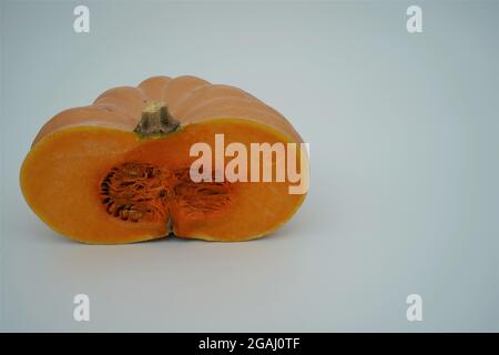 Die Hälfte eines Butternusskürbis oder Kürbisses mit viel Kopierraum isoliert. Saisonales Gemüse in leuchtendem Orange im Kontrast zum Hintergrund. Stockfoto