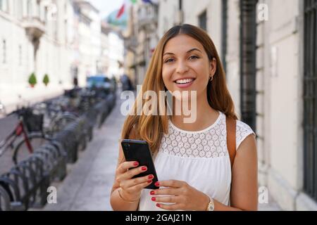 Lässige Frau mit Mobiltelefon und Blick auf die Kamera im Freien Stockfoto