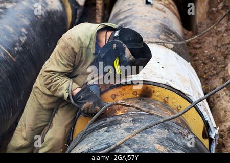 Reparatur des Heizkanals. Die Arbeiter, Schweißer, die durch Elektroschweißen und Gasschweißen an großen Eisenrohren in einer Tiefe von ausgegrabenen Graben hergestellt wurden. Stockfoto