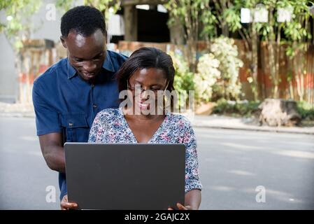 Junges Paar im Freien, das lächelnd auf den Laptop schaut. Stockfoto