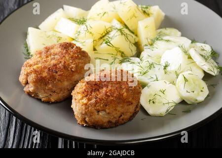 Kotlety Mielone sind traditionelle polnische, in der Pfanne gebratene Fleischpasteten, serviert mit gekochten Kartoffeln und Gurkensalat in der Nähe auf dem Teller auf dem Tisch. Horizont Stockfoto