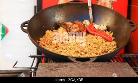 Köstlicher usbekischer Pilaf in einem Kessel im Freien auf einem Street Food Festival. Kochen von Reis mit Fleisch und Gemüse. Ein großer Topf von nationalen kasachischen c Stockfoto