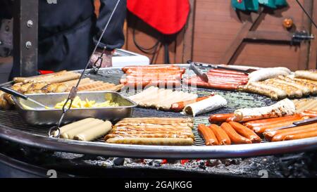 Gebratene Würstchen. Straßenrestaurant. Viele gegrillte Würstchen auf einem großen runden Grill auf einem Street Food Festival. Barbecue-Grill am Food-Stand Weihnachten Stockfoto