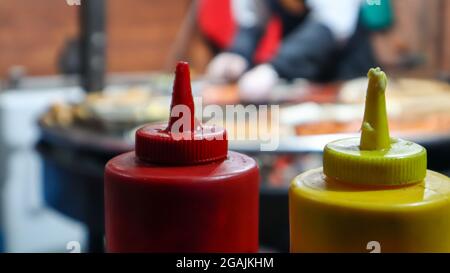 Ketchup und Mayonnaise in Kunststoffrohren in der Nähe eines Straßengrills im Vordergrund, Nahaufnahme mit selektivem Fokus. Barbecue, Street Food Festival. Zwei Dosen Stockfoto