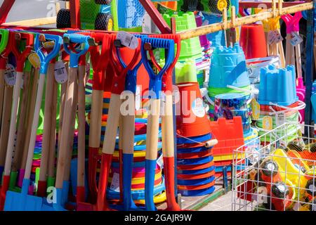 Bunte Kinder-Plastikeimer und -Spaten; Strandspielzeug zum Verkauf am Meer in Großbritannien. Stockfoto