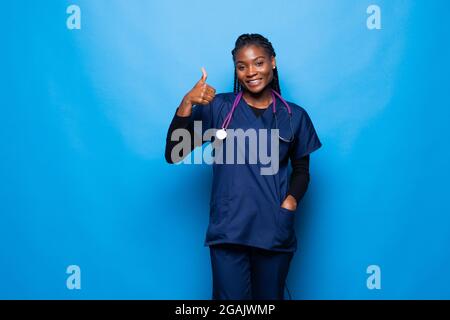 Vorderansicht der afroamerikanischen Krankenschwester mit Daumen nach oben lächelnd isoliert auf Weiß Stockfoto