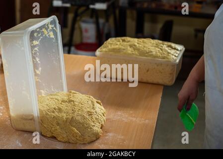 Mujer caucásica masando masa para hacer pan y bizcochos en una mesa color madera con luz de día, en una panadería. Stockfoto