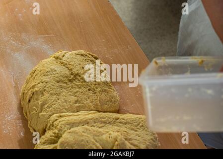 Mujer caucásica masando masa para hacer pan y bizcochos en una mesa color madera con luz de día, en una panadería. Stockfoto