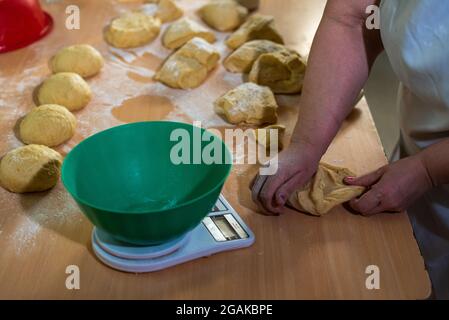 Mujer caucásica masando masa para hacer pan y bizcochos en una mesa color madera con luz de día, en una panadería. Stockfoto