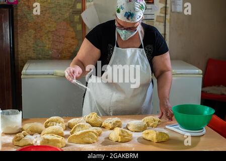 Mujer caucásica masando masa para hacer pan y bizcochos en una mesa color madera con luz de día, en una panadería. Stockfoto