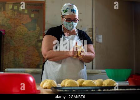 Mujer caucásica masando masa para hacer pan y bizcochos en una mesa color madera con luz de día, en una panadería. Stockfoto