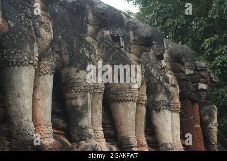 Elefantenstatuen um die Basis (Chedi) eines alten buddhistischen Tempels im Kamphaeng Phet Historical Park, Thailand Stockfoto