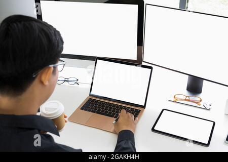 Rückansicht Geschäftsmann trinkt Kaffee und arbeitet mit mehreren modernen Gadgets im Büro. Stockfoto