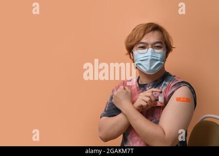 Asiatischer Mann, der nach dem Impfen den Arm mit Gips zeigt. Stockfoto